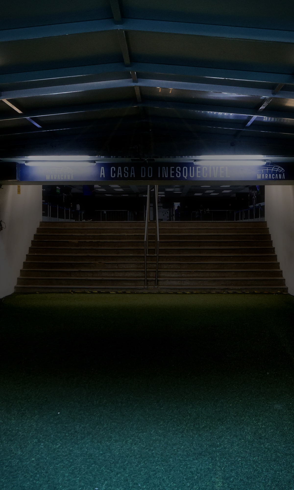 Túnel de acesso à arquibancada do Maracanã, com a escada iluminada ao centro e a placa "A casa do inesquecível" ao fundo.
