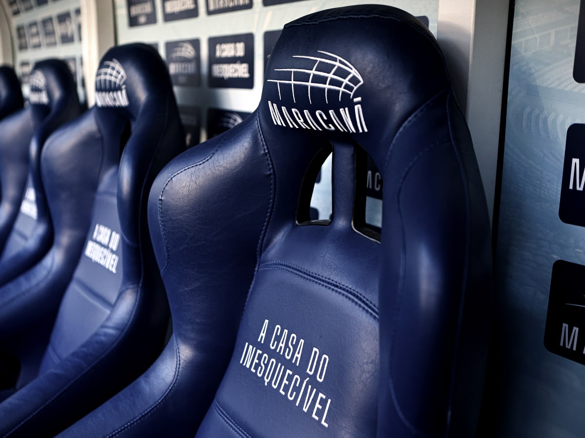 Fileira de poltronas azuis do banco de reservas do Maracanã, com o escudo do estádio e a frase "A casa do inesquecível" bordados no encosto.