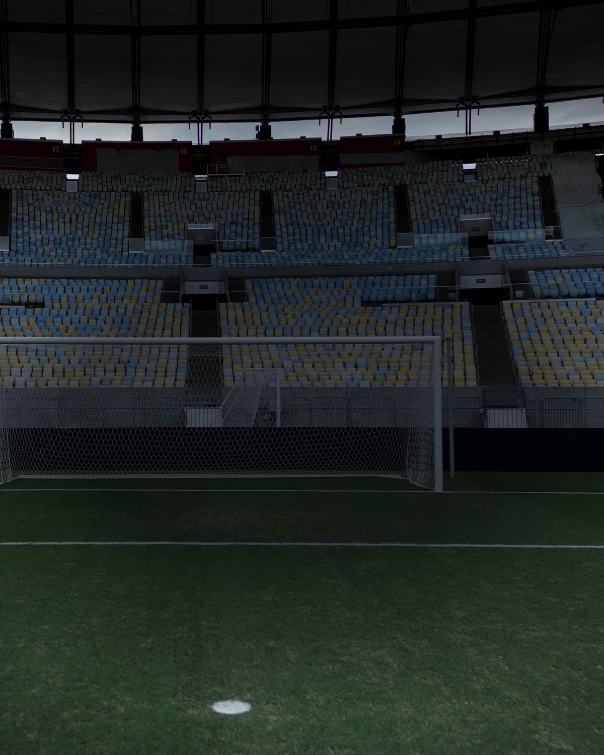 O gol do Maracanã visto rente ao gramado, com a rede em primeiro plano e as arquibancadas azuis e amarelas vazias atrás.