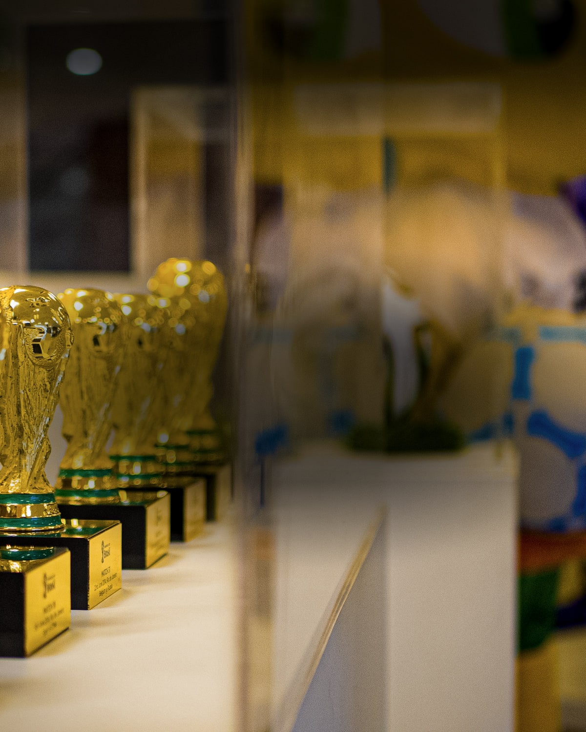 Fileira de troféus dourados em miniatura numa vitrine iluminada, com as placas na base fora de foco.