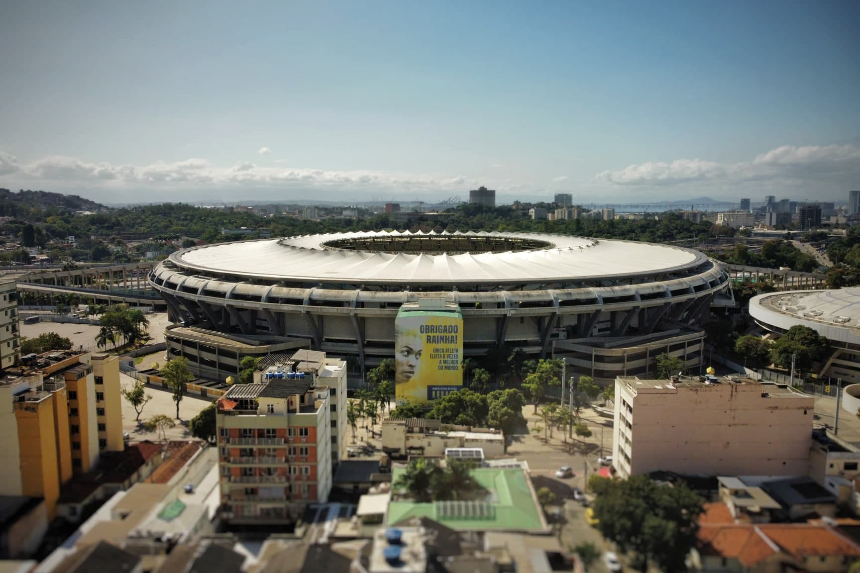 O Maracanã visto do alto em dia claro, com a cobertura branca em anel, os prédios do bairro em volta e o horizonte da cidade ao fundo.
